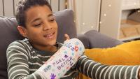 Smiling boy with a decorated arm cast taking a selfie on the couch.